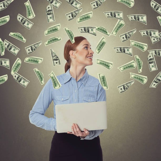 successful businesswoman holding laptop and looking at raining dollar bills